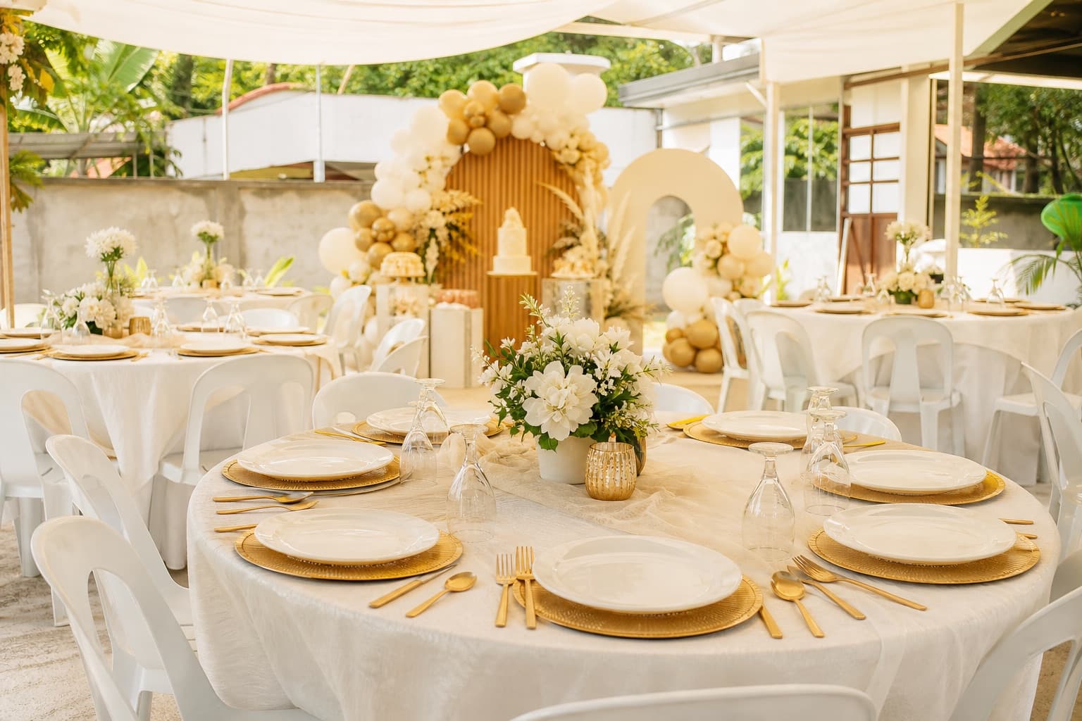 Outdoor celebration setup with white tables, chairs, and warm gold accents